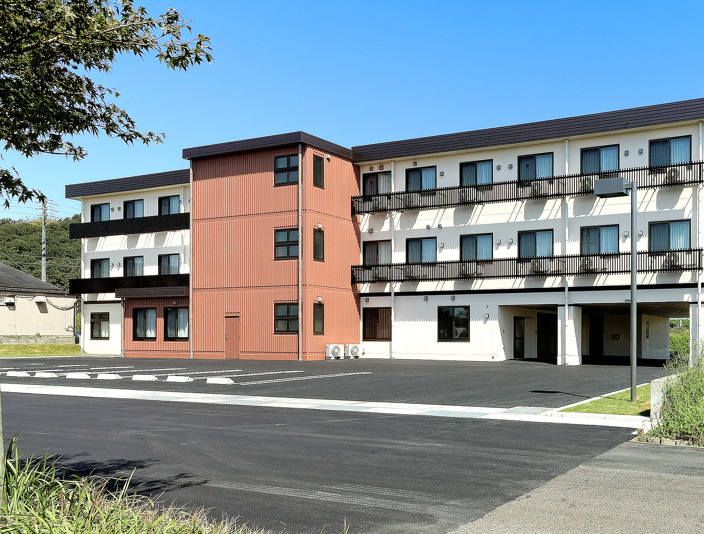 介護施設の建物外観。赤茶色と白を基調とした3階建ての近代的な施設で、駐車場から見た全景。